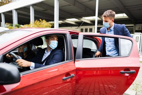 Business man steps into a rideshare vehicle while wearing a face mask during the day