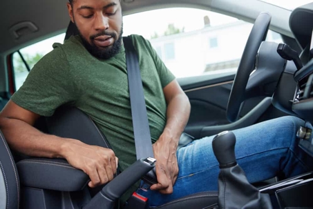 Man buckles his seat belt while sitting in the driver's seat of a car
