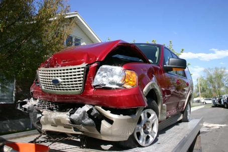 Red SUV with a smashed front end sits atop a tow truck during the day