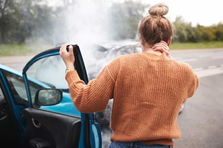Young woman grasps the back of her neck with her hand as she gets out of the passenger side of a vehicle after a rear-end collision