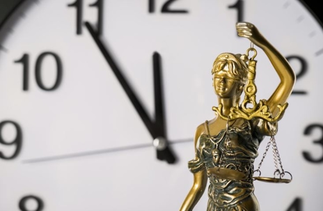 Lady Justice statue in front of analog clock