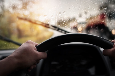 person behind wheel of car driving in the rain