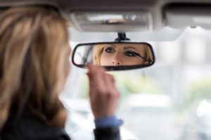woman using rearview mirror to apply mascara