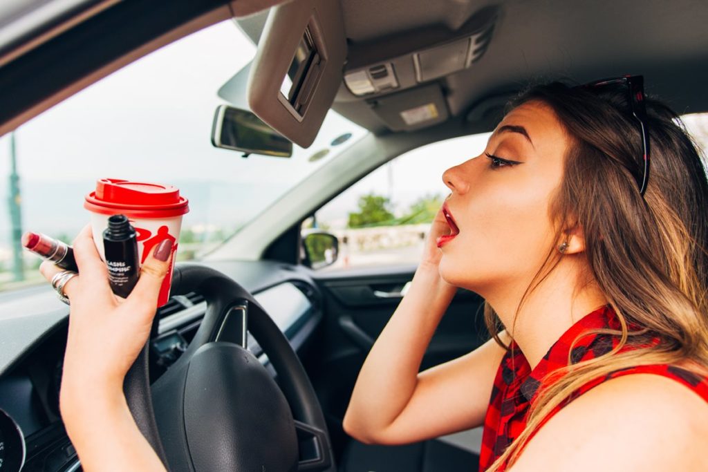 woman putting on makeup and drinking coffee while driving