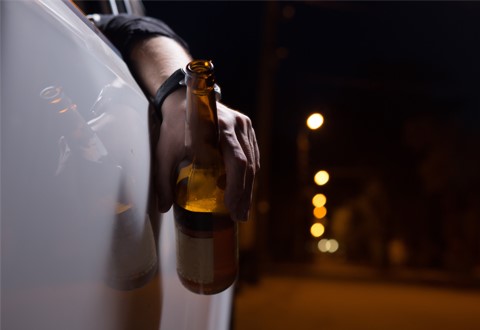 drunk driver hanging arm out window with beer bottle